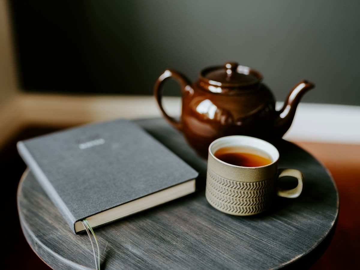A cup of tea, a teapot and a notebook on a small side table