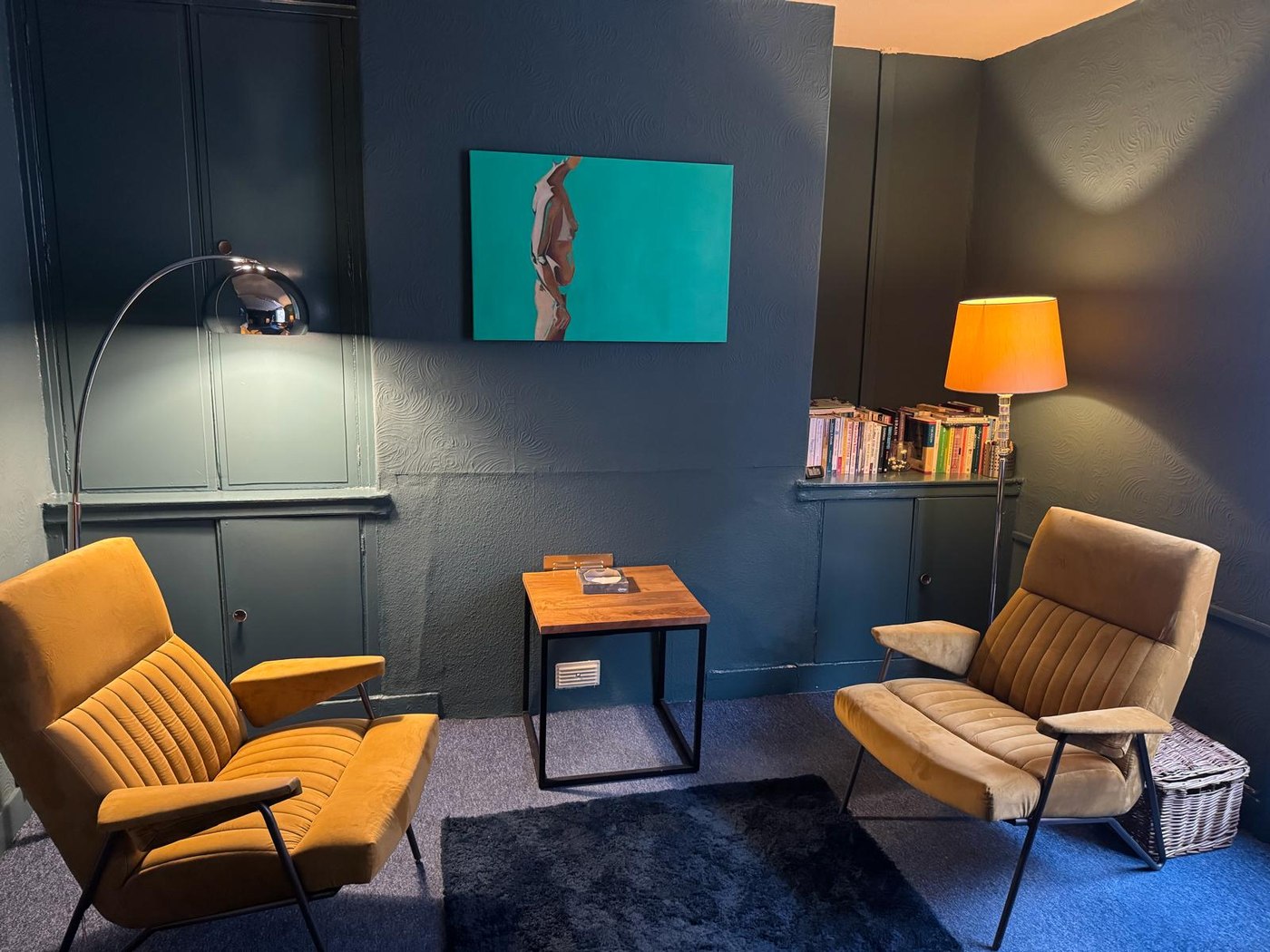 The counselling room at Claremont Counselling, with two mid-century armchairs, warm lamplight and a bookshelf
